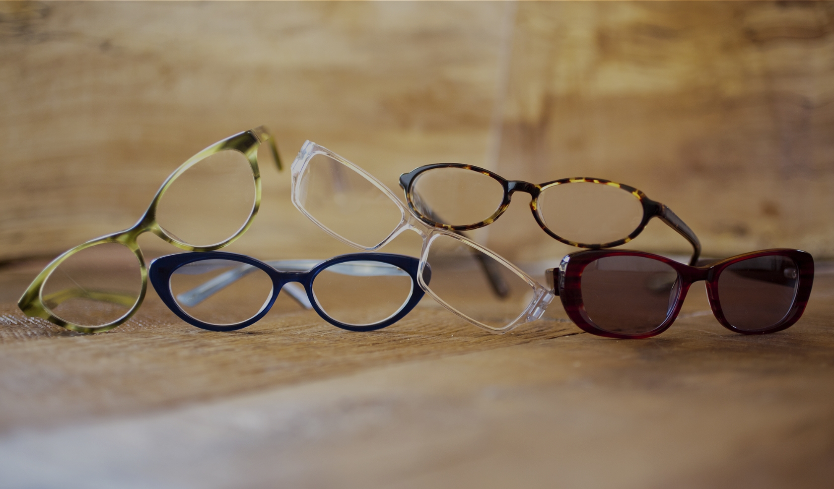 Five pairs of glasses stacked on a wooden surface