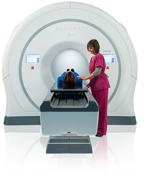 A nurse standing next to a patient laying on a table waiting to be slid into a machine from Accuray