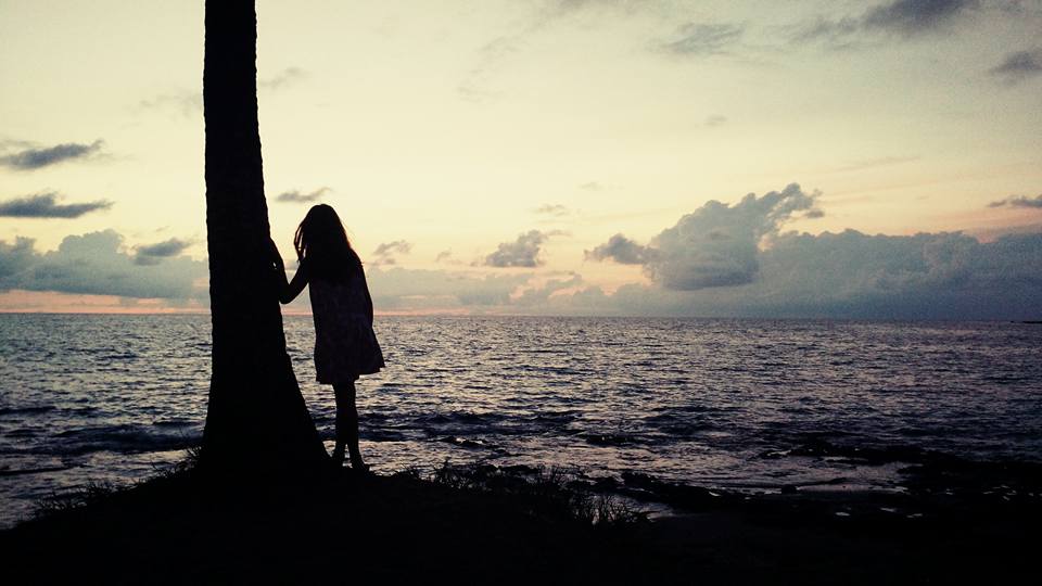 Girl leaning on palm tree, backlit by sunset on the beach